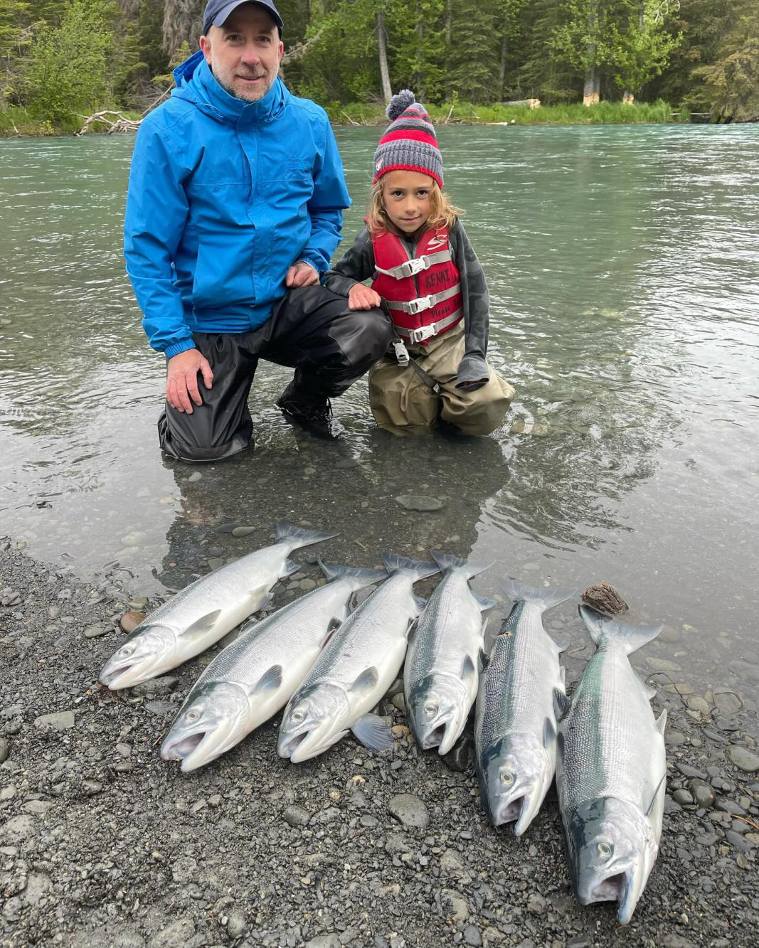 A child sits next to a fishing guide, excitedly looking at Sockeye Salmon from the Kenai River, Alaska.