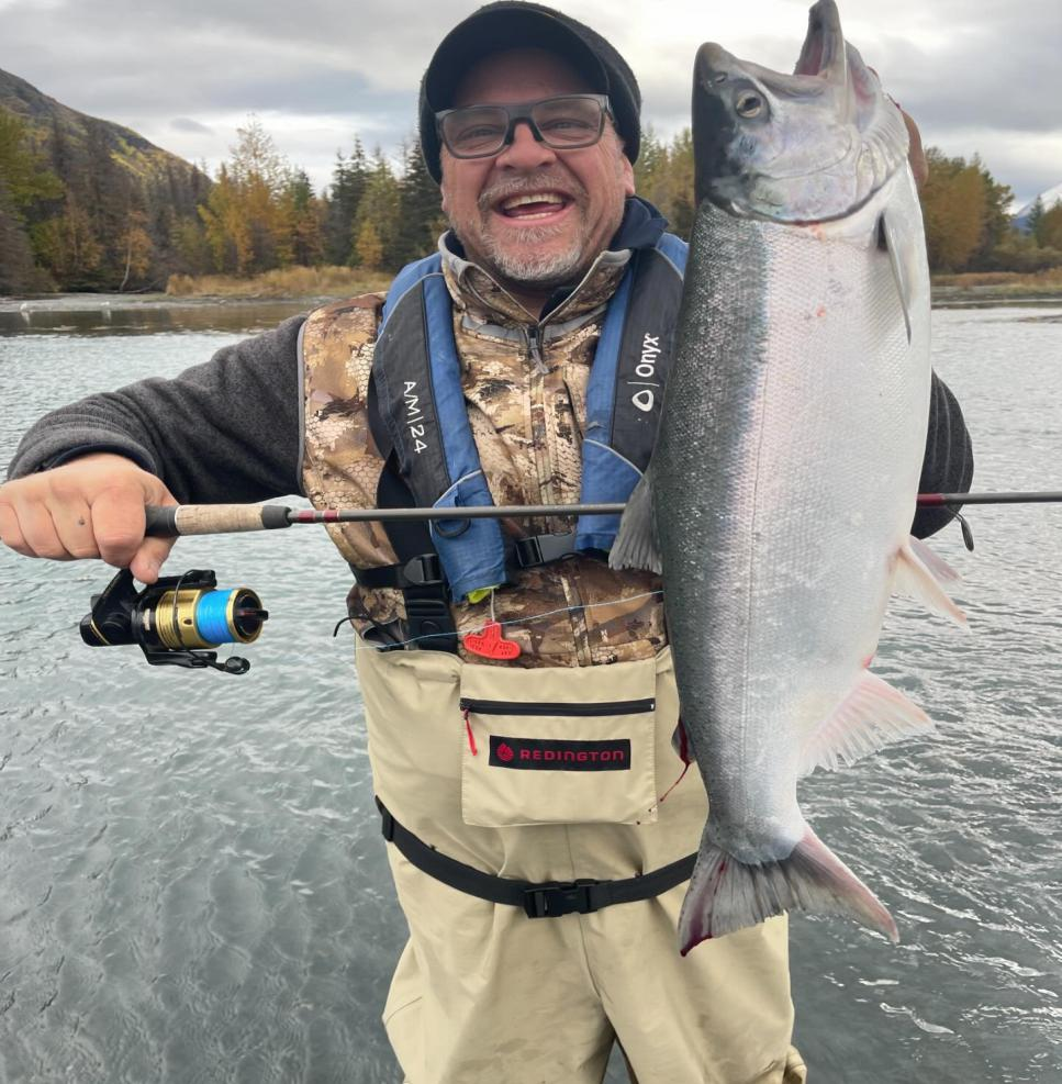 A smiling angler holds up a bright Sockeye Salmon caught on the Kenai River