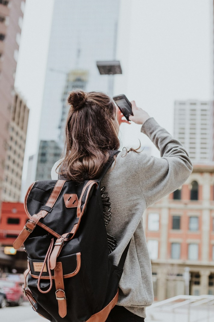 Woman wearing a bag, capturing a picture in a city’s downtown